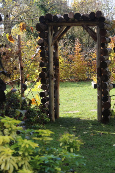 Pergola en rondins de bois ouvrant sur un jardin paysager verdoyant.