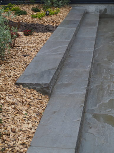 Marches et palis en grès posés dans un jardin paysager avec paillage et massifs végétalisés.