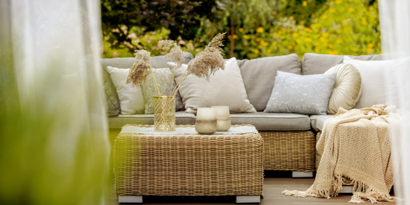 amenagement-salon-exterieur-rotin-deco-jardin Salon d’extérieur cosy avec canapé en rotin, table basse assortie et coussins beiges, dans un jardin verdoyant.