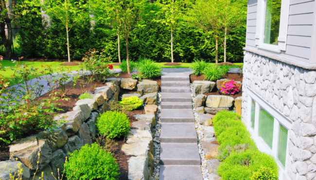 amenagement-exterieur-escalier-jardin-paysager Aménagement extérieur paysager avec escalier en pierre, massifs fleuris et arbustes, autour d’une maison en pierre.